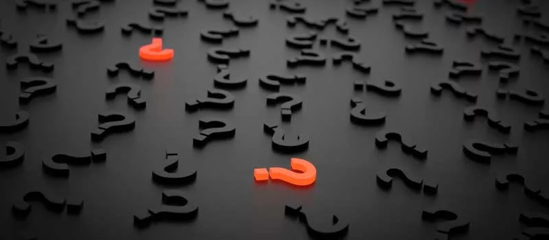Signos de interrogación negros sobre fondo oscuro con uno naranja destacado